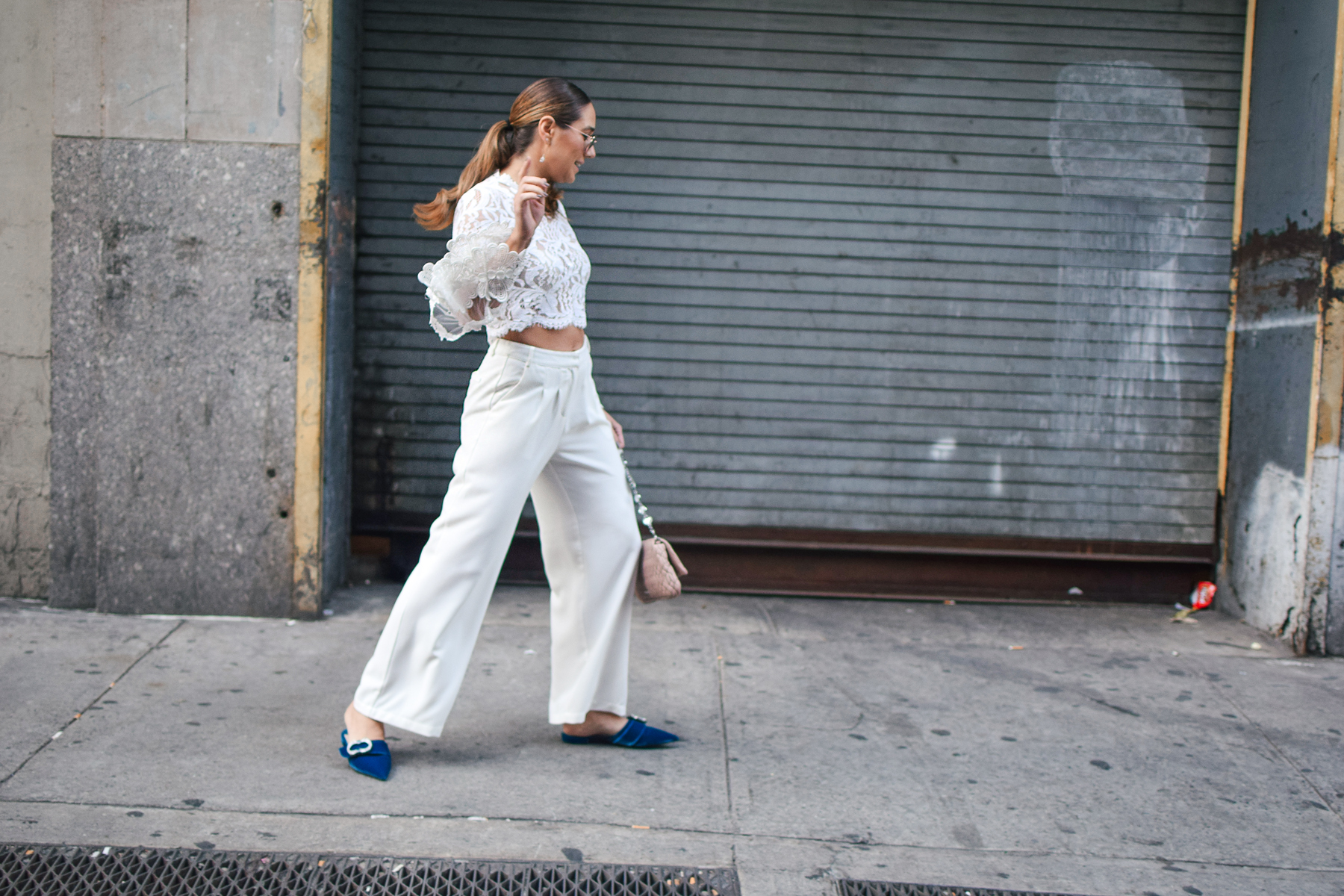 nyfw-streetstyle-outfit-lace-ruffle-statement-bell-sleeve-blouse-white-trousers-all-white-prada-royal-blue-slides-blush-accessories-candid-shot